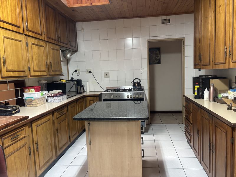 A functional kitchen featuring wooden cabinetry, granite countertops, a central island, and a gas stove with a tiled backsplash and flooring.