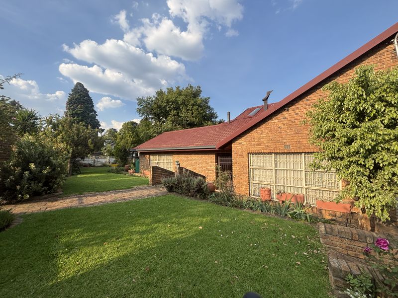 A view of the rear exterior featuring a face brick facade, pitched metal roof, and a well-maintained garden with a brick pathway.