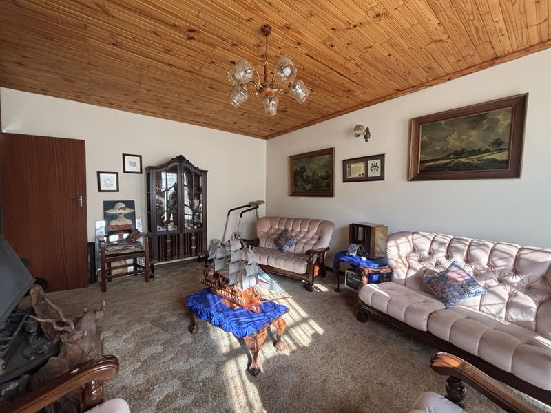 A traditional living room featuring a warm timber tongue and groove ceiling, carpeted flooring, and a built-in fireplace.