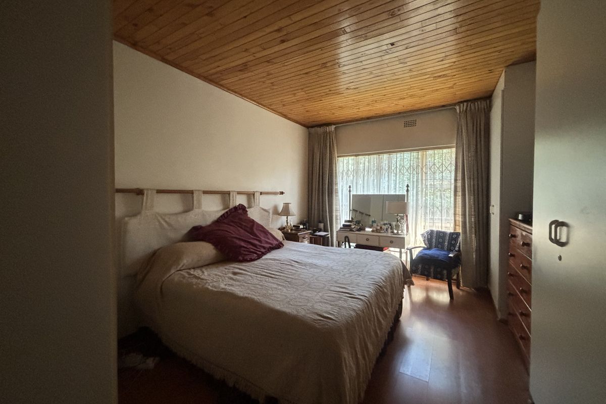 A bedroom featuring a timber-clad ceiling, laminate flooring, and a large window fitted with a security gate.
