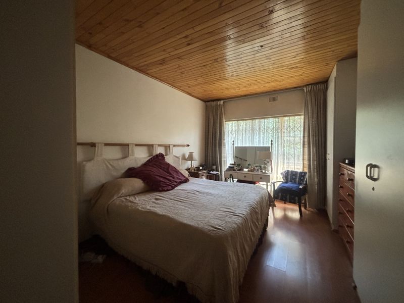 A bedroom featuring a timber-clad ceiling, laminate flooring, and a large window fitted with a security gate.