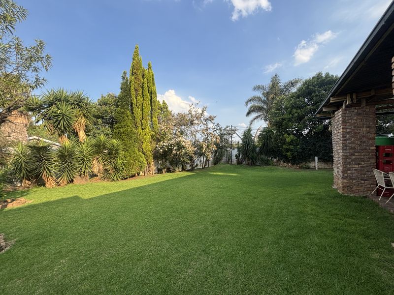 A well-maintained, spacious green lawn garden featuring mature trees and a brick exterior wall of the house.