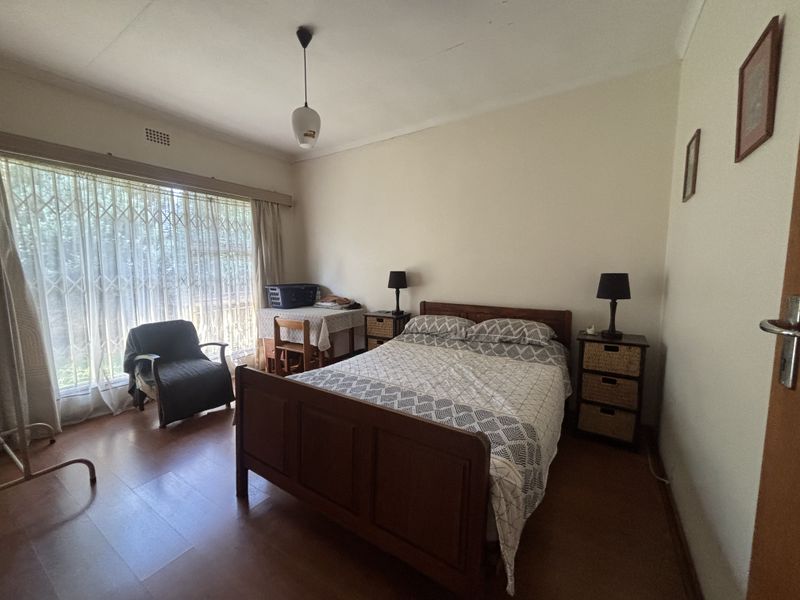 A standard bedroom featuring laminate flooring, a large window with security gate, and neutral wall finishes.