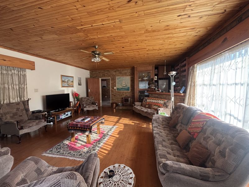 Spacious living room featuring warm timber ceilings, hardwood flooring, an exposed brick feature wall, and a built-in bar area.
