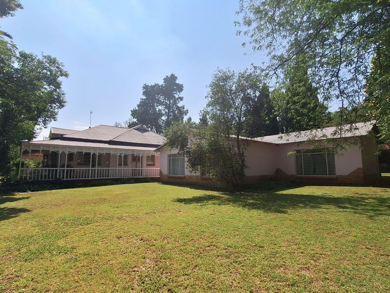 A view of the rear elevation of the house, featuring a covered veranda, large lawn, and established garden surroundings.