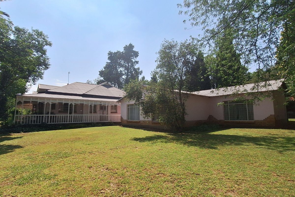 A view of the rear elevation of the house, featuring a covered veranda, large lawn, and established garden surroundings.