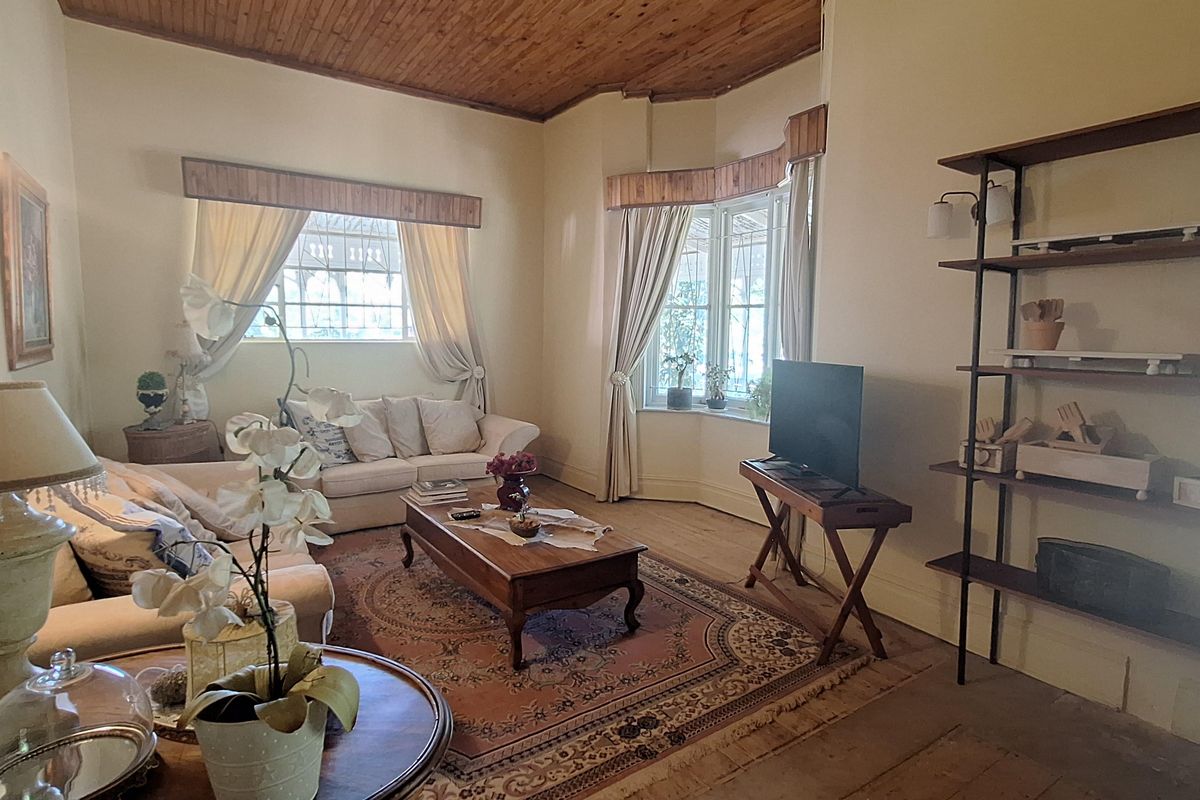 A spacious living room featuring a high timber-clad ceiling, large bay windows, and original timber flooring, offering a warm and traditional aesthetic.