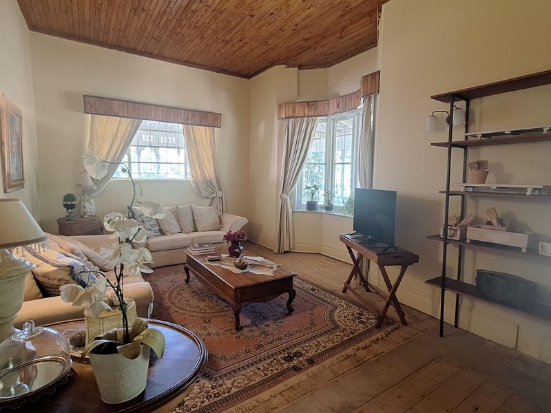 A spacious living room featuring a high timber-clad ceiling, large bay windows, and original timber flooring, offering a warm and traditional aesthetic.