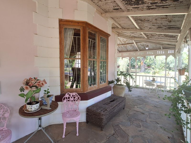 A covered patio featuring natural stone flooring, a bay window, and decorative timber fretwork, offering a view of the garden.