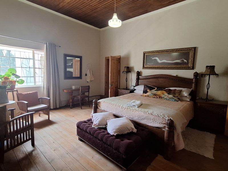 Spacious bedroom featuring high timber-paneled ceilings, original hardwood flooring, and large windows with security bars, offering a classic and character-filled living space.