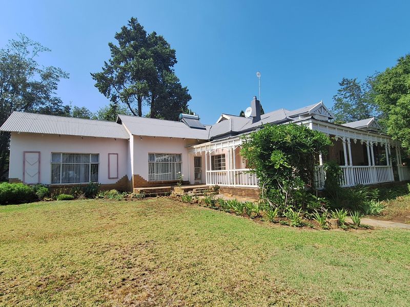 A charming single-story house featuring a covered veranda, corrugated metal roof, and a spacious front garden with established landscaping.