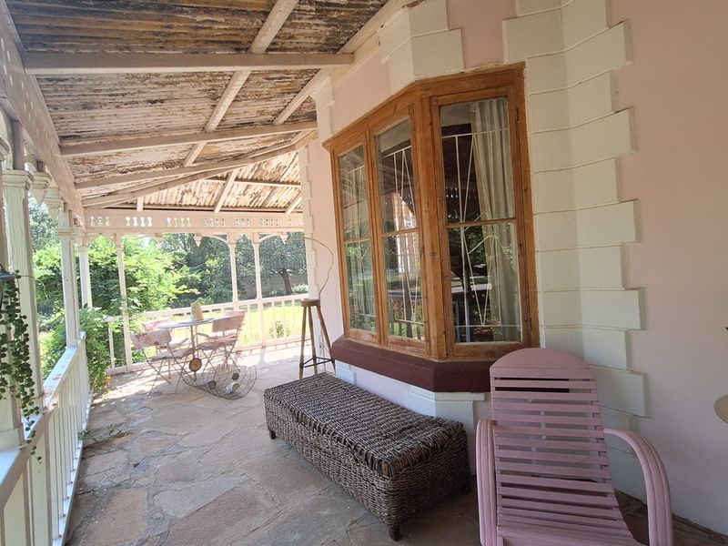 A covered veranda featuring stone flooring, timber-framed bay windows, and a weathered corrugated iron roof, offering a rustic outdoor living space.