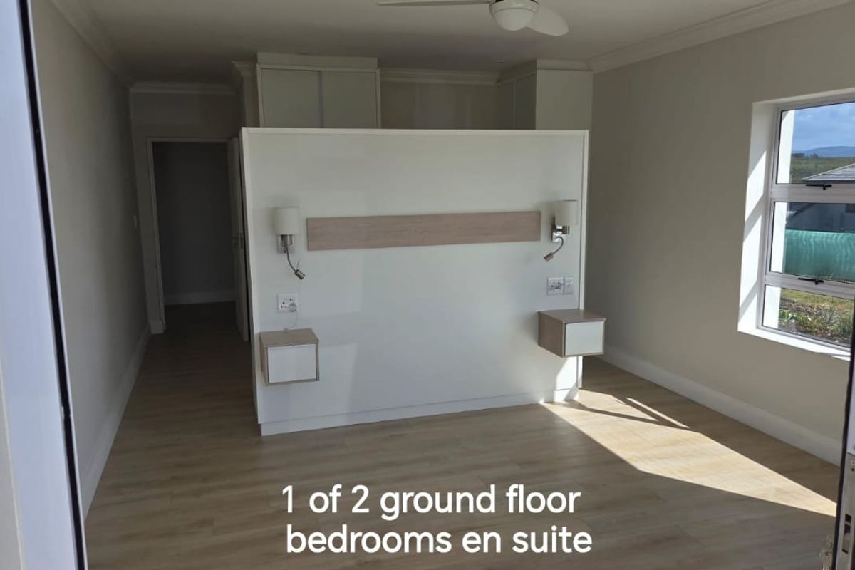 A modern, bright ground floor bedroom featuring a central partition wall with integrated headboard, floating bedside tables, and built-in storage.