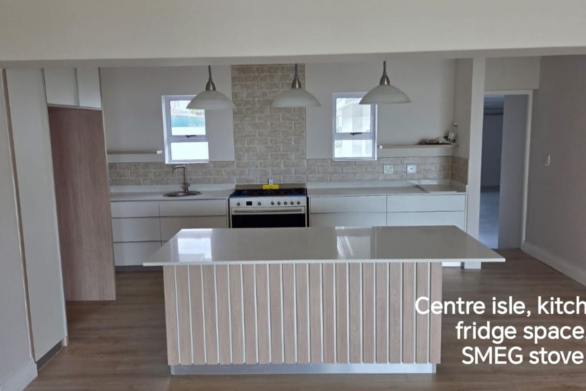 Modern kitchen featuring a central island, stone countertops, gas stove, and integrated cabinetry with a neutral tiled backsplash.