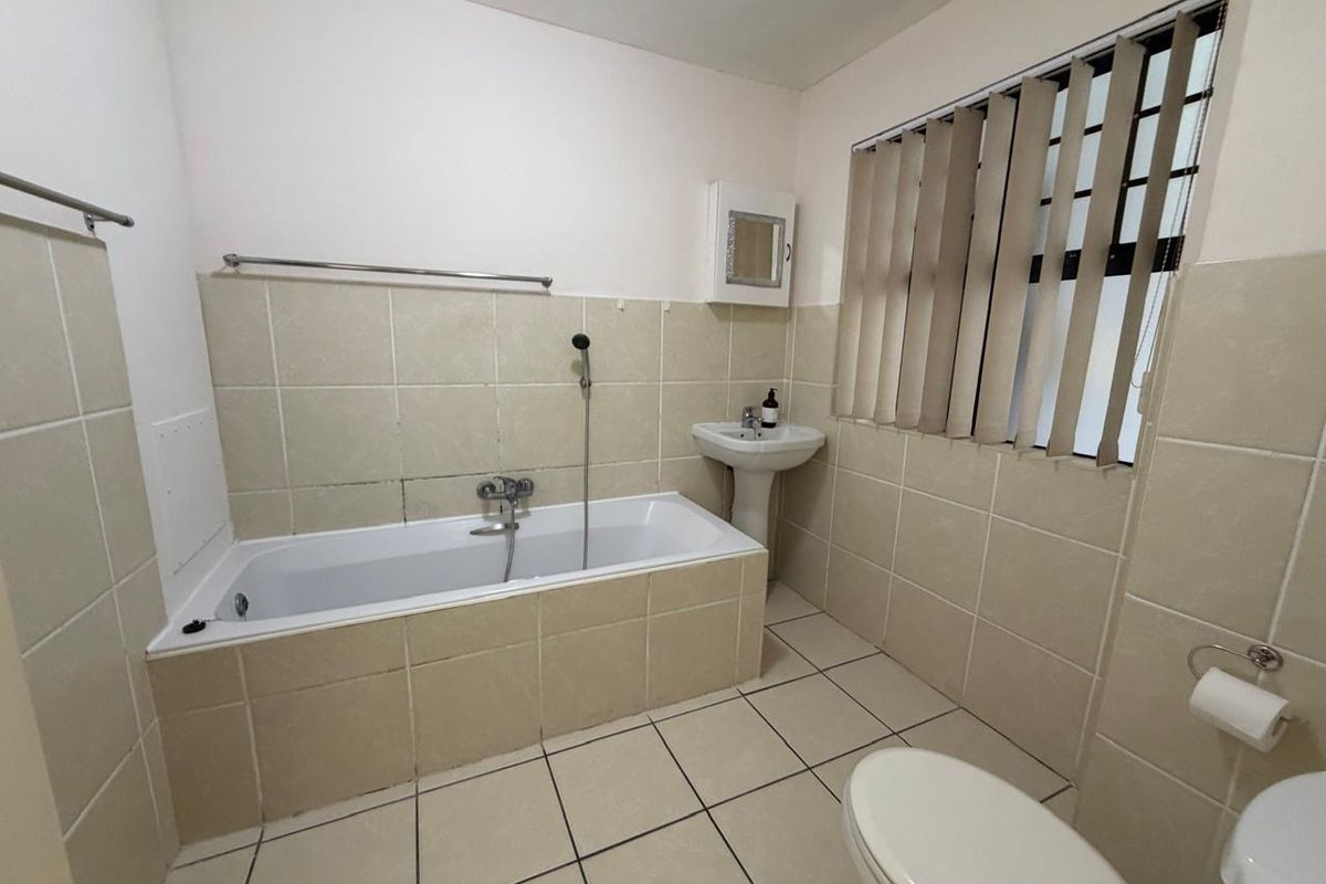 A functional bathroom featuring a bathtub, pedestal basin, toilet, and neutral tiled finishes throughout.