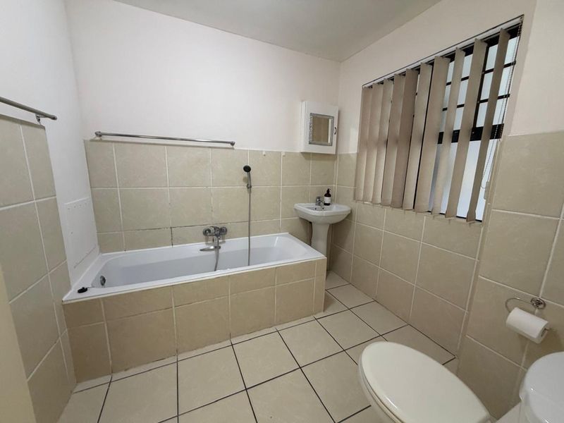 A functional bathroom featuring a bathtub, pedestal basin, toilet, and neutral tiled finishes throughout.