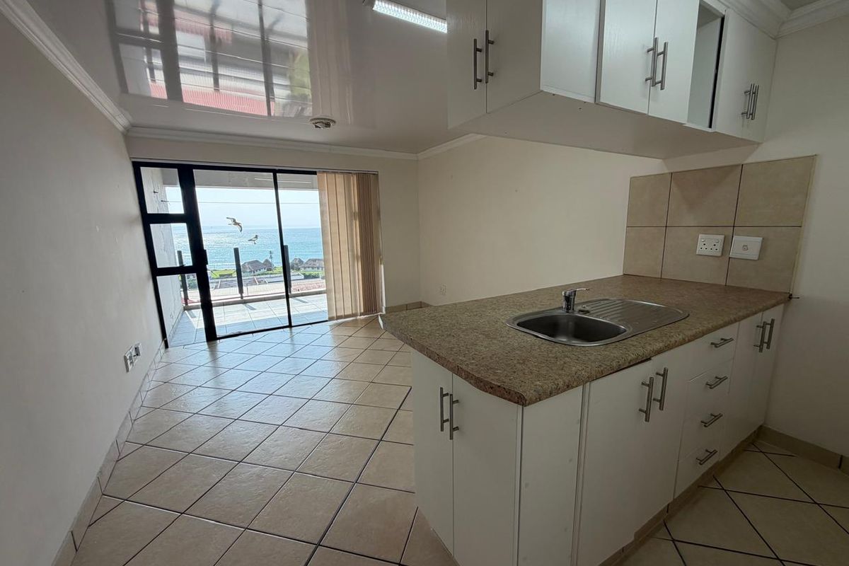 Open-plan kitchen and living area featuring tiled floors, built-in cabinetry, and a sliding door leading to a balcony with ocean views.