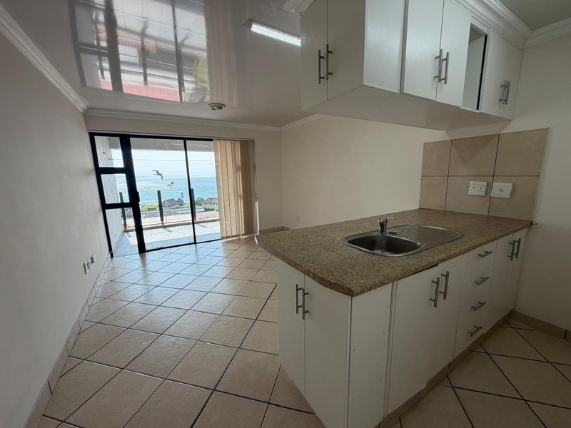 Open-plan kitchen and living area featuring tiled floors, built-in cabinetry, and a sliding door leading to a balcony with ocean views.
