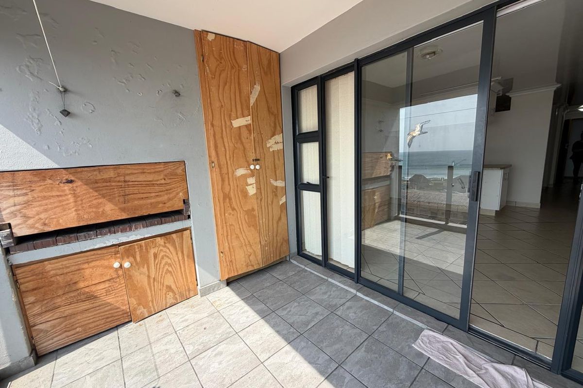 Covered balcony featuring a built-in braai, tiled flooring, and sliding glass doors providing access to the interior living space.