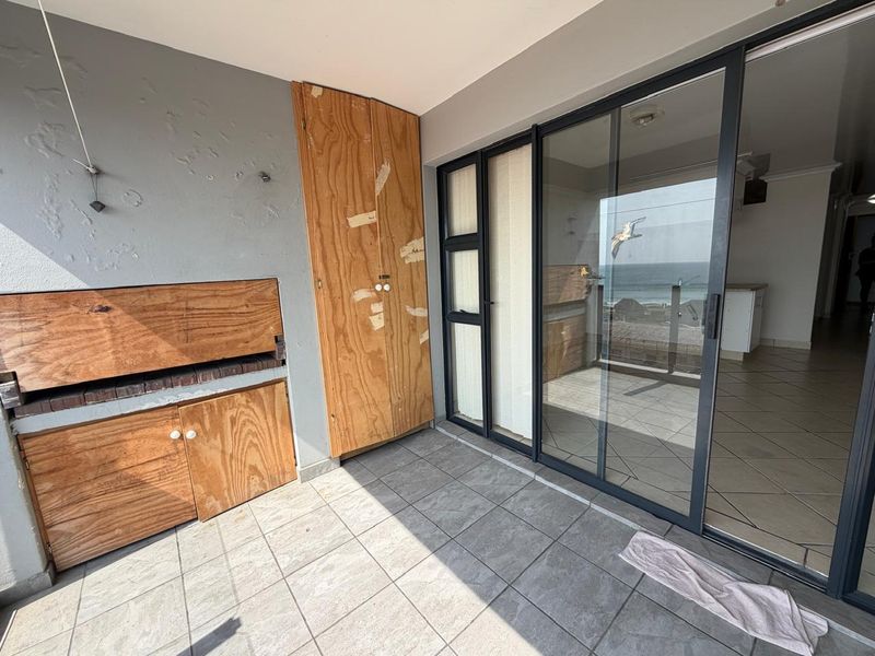 Covered balcony featuring a built-in braai, tiled flooring, and sliding glass doors providing access to the interior living space.