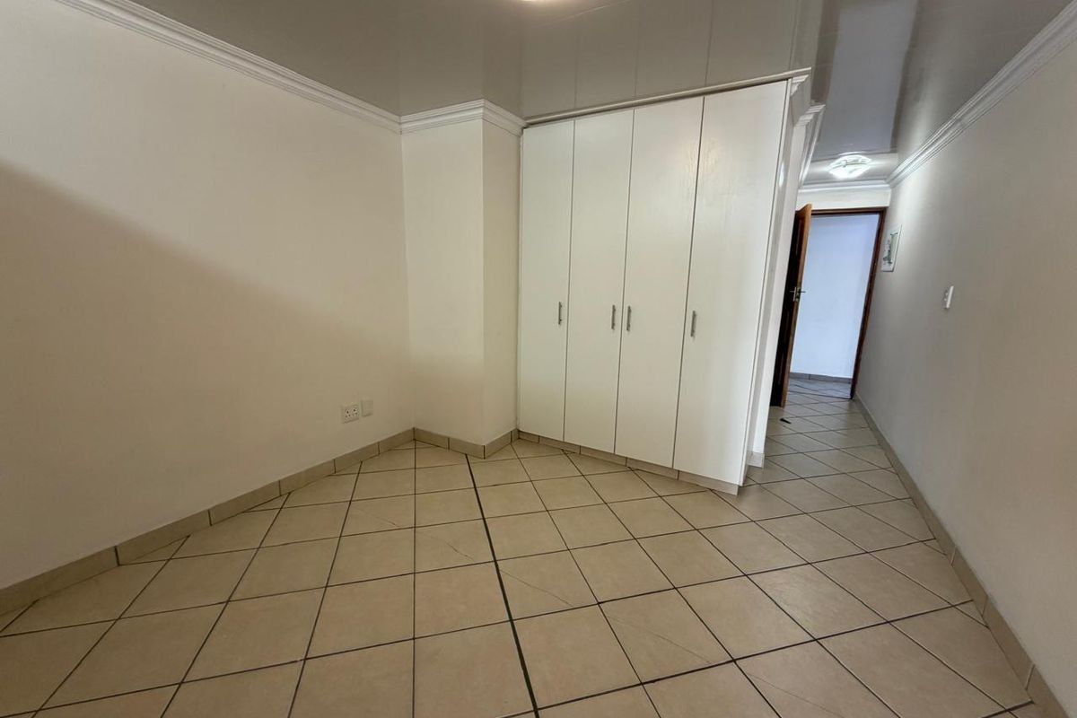 A clean, empty bedroom featuring neutral tiled flooring, built-in white cupboards, and coved cornicing, offering a versatile space ready for personalization.