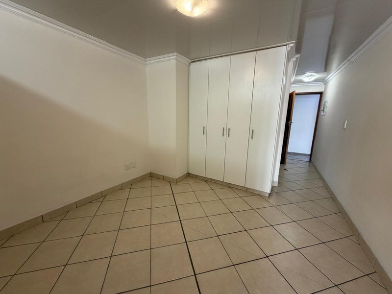 A clean, empty bedroom featuring neutral tiled flooring, built-in white cupboards, and coved cornicing, offering a versatile space ready for personalization.
