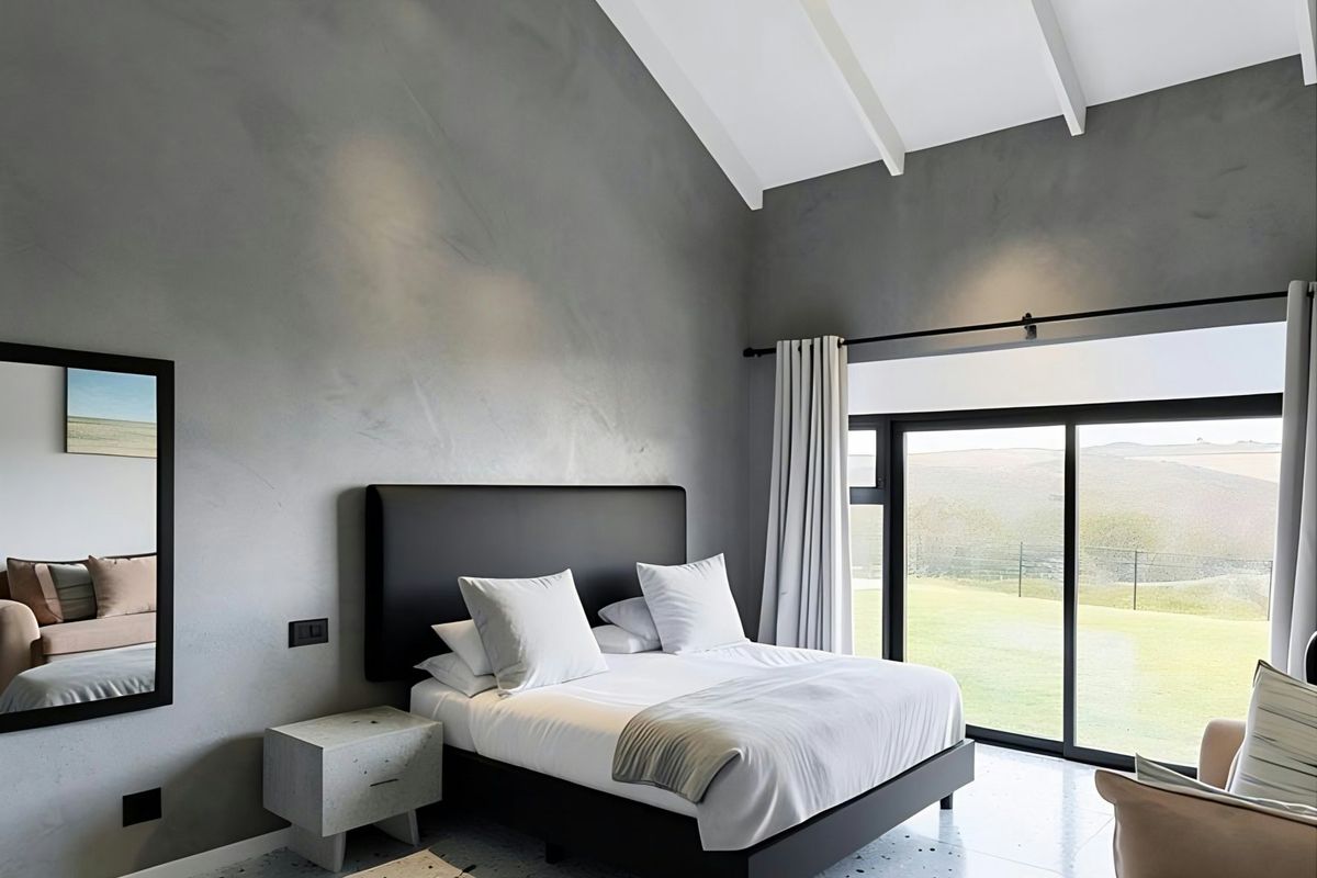 Modern bedroom featuring a high vaulted ceiling with exposed beams, terrazzo flooring, and large sliding glass doors offering scenic landscape views.