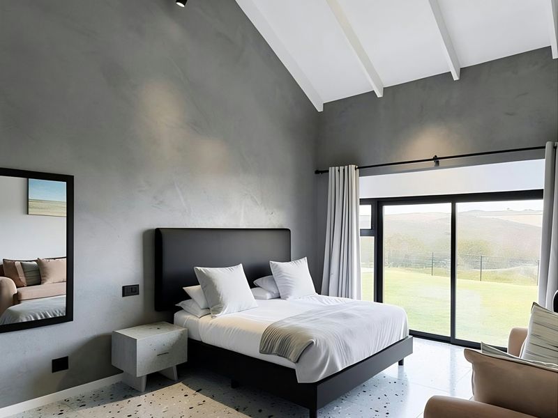 Modern bedroom featuring a high vaulted ceiling with exposed beams, terrazzo flooring, and large sliding glass doors offering scenic landscape views.