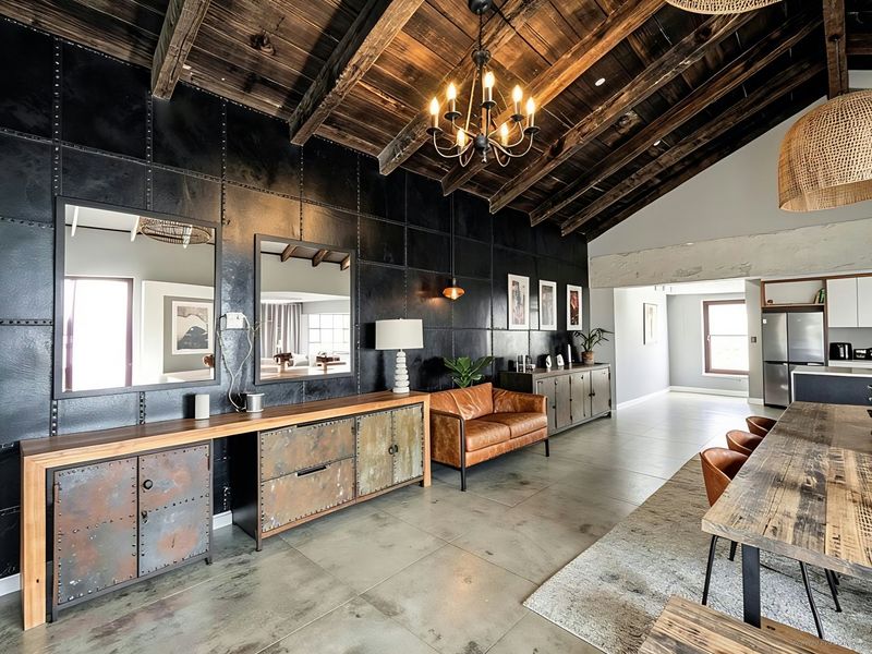 Spacious open-plan living area featuring industrial-style metal wall cladding, exposed timber ceiling beams, and polished concrete floors with a modern aesthetic.
