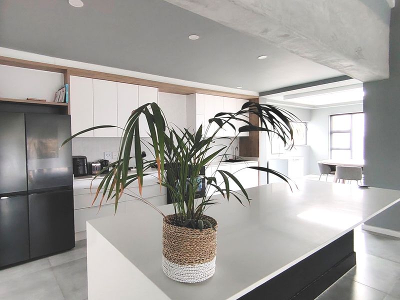 Modern open-plan kitchen featuring a large central island, sleek white cabinetry, and contemporary finishes with an exposed structural beam.