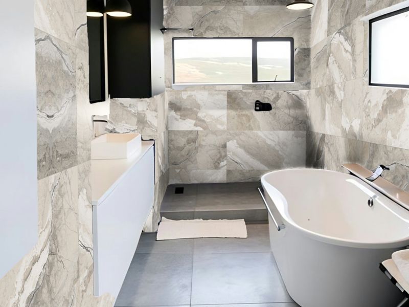 Modern bathroom featuring large-format marble-effect wall tiles, a sleek wall-mounted vanity with vessel sink, and a contemporary freestanding bathtub with a walk-in shower area.