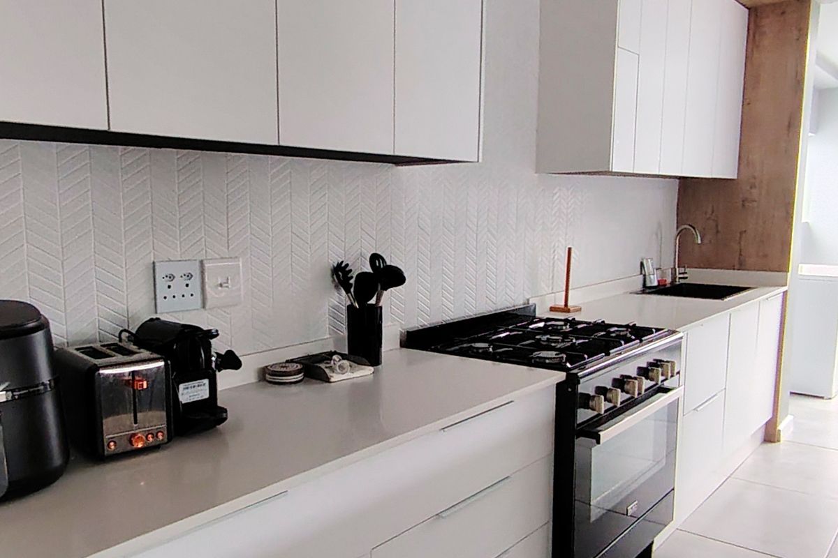 Modern kitchen featuring sleek white cabinetry, stone countertops, a gas stove with oven, and a stylish herringbone tiled backsplash.