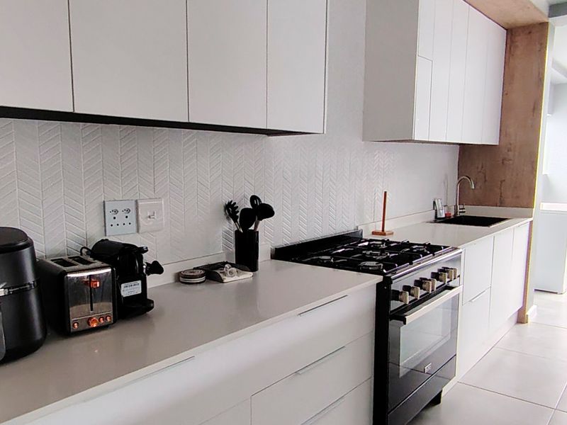 Modern kitchen featuring sleek white cabinetry, stone countertops, a gas stove with oven, and a stylish herringbone tiled backsplash.