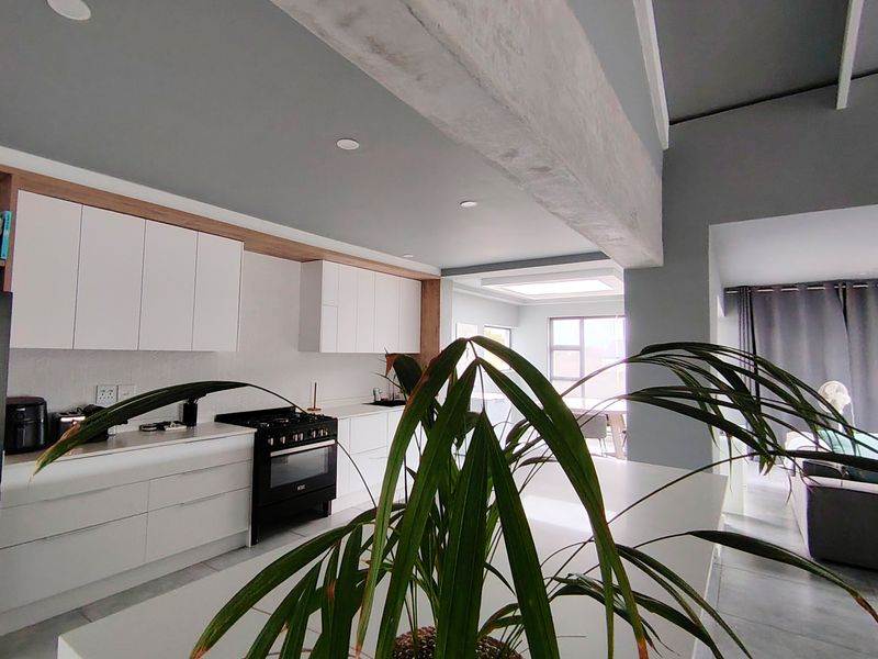 Modern open-plan kitchen featuring sleek white cabinetry, stone countertops, a gas stove, and an exposed concrete beam, seamlessly flowing into the living area.