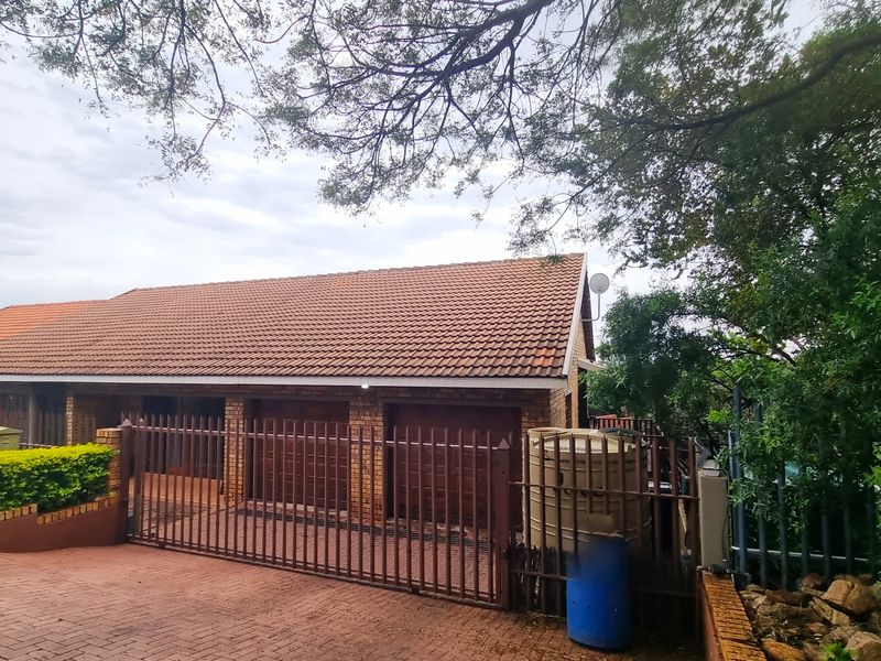 Exterior view of the property featuring a brick facade, tiled roof, double garage, and secure metal perimeter fencing.