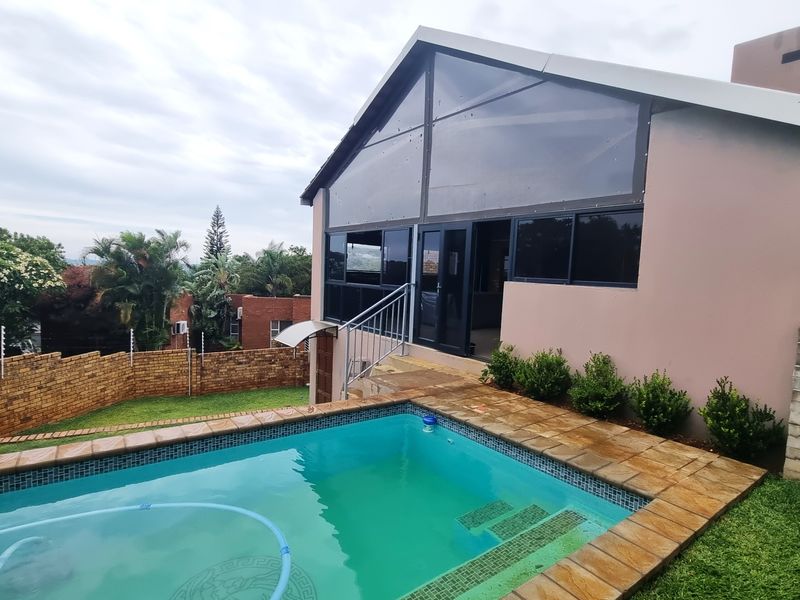 Rear view of the property featuring a swimming pool, paved surround, and a modern architectural design with large glass windows.