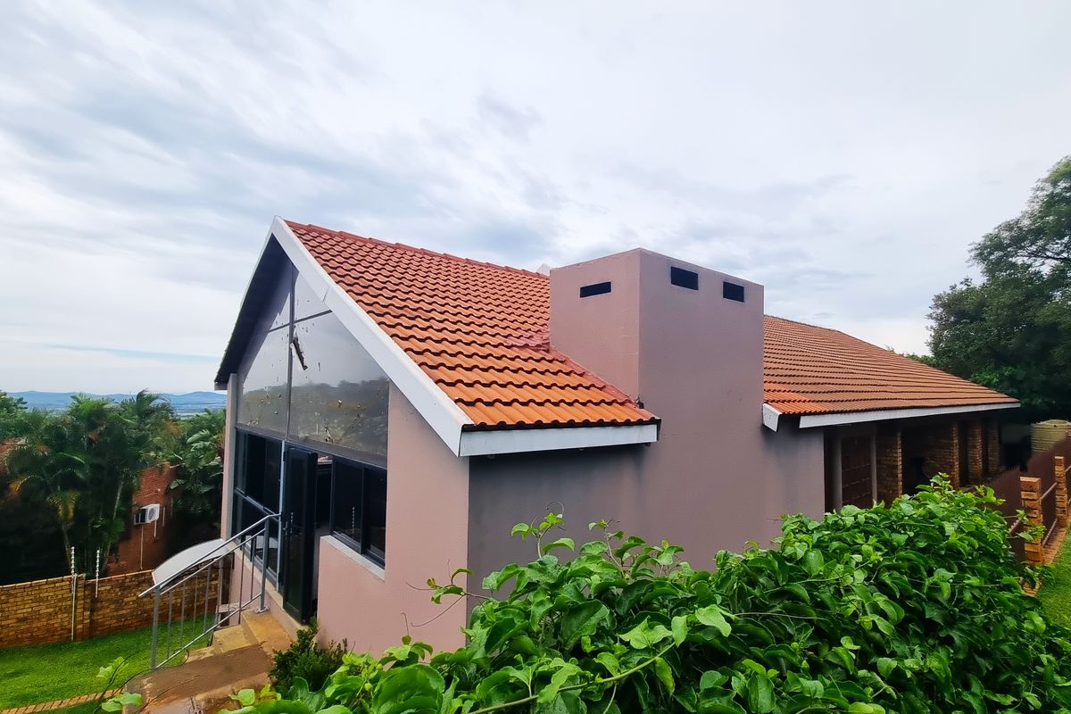 A side view of the house featuring a pitched terracotta tiled roof, a prominent chimney stack, and large glass windows overlooking the garden.