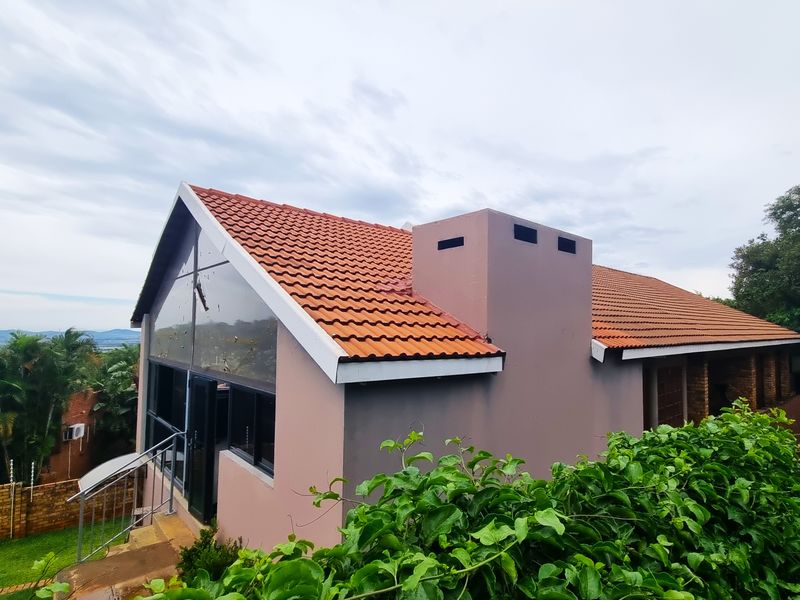 A side view of the house featuring a pitched terracotta tiled roof, a prominent chimney stack, and large glass windows overlooking the garden.