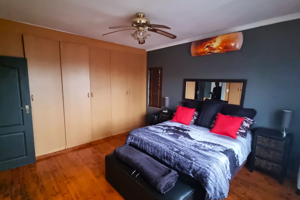 A bedroom featuring built-in wooden wardrobes, polished wooden flooring, and a ceiling fan.