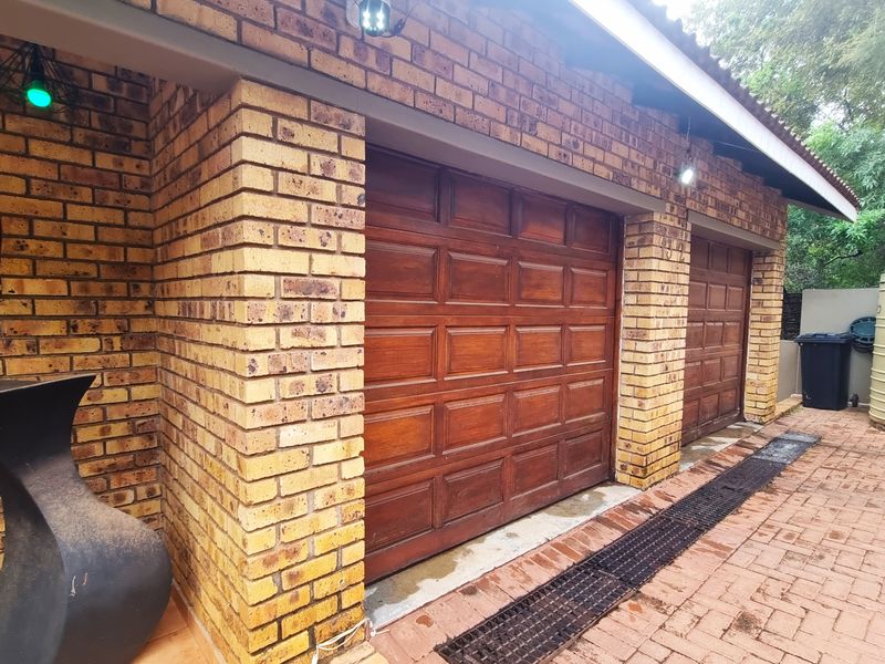 A double garage featuring face-brick construction and traditional timber sectional doors, complemented by paved driveway and an external water storage tank.
