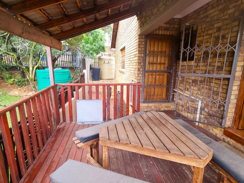 Covered timber deck patio featuring a brick exterior wall, security gate, and access to the rear garden area with water storage tanks.