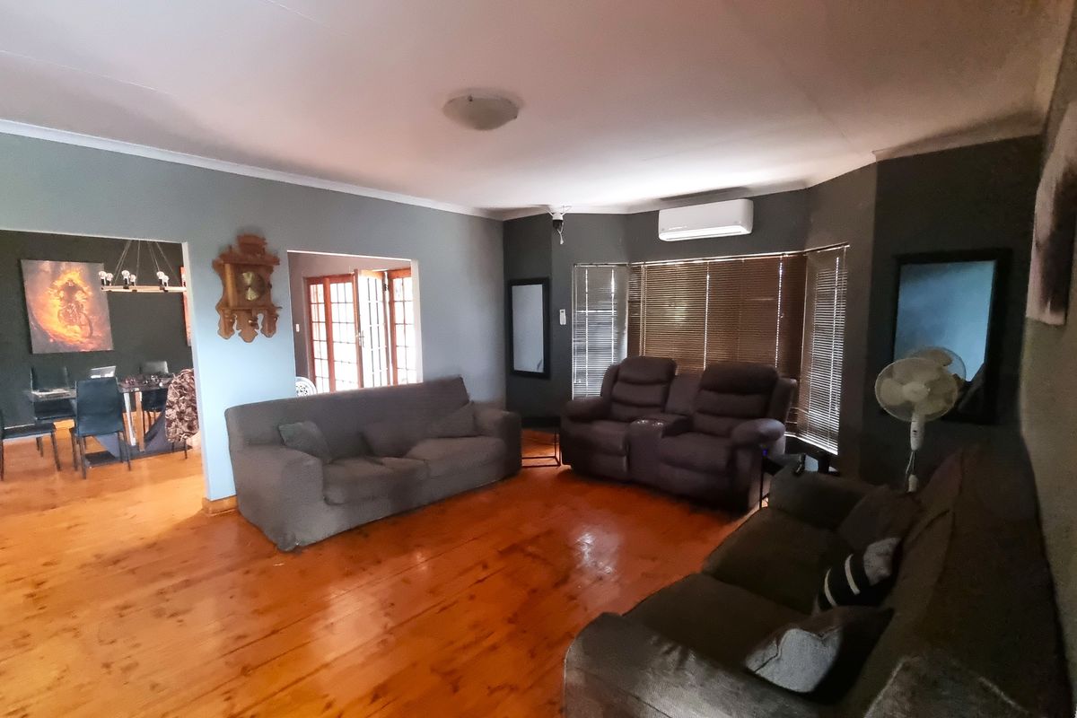 Spacious living room featuring polished timber flooring, a wall-mounted air conditioning unit, and large windows with fitted blinds, leading into an adjacent dining area.