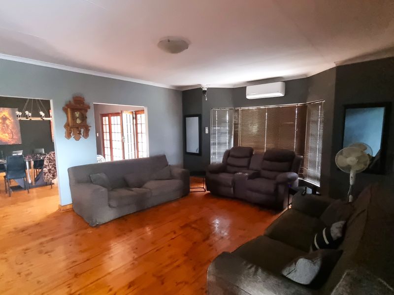 Spacious living room featuring polished timber flooring, a wall-mounted air conditioning unit, and large windows with fitted blinds, leading into an adjacent dining area.