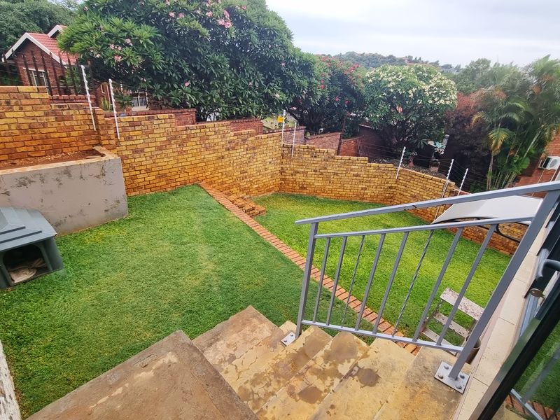 A private rear garden featuring a lawn, brick boundary walls with electric fencing, and concrete stairs leading down from the main dwelling.