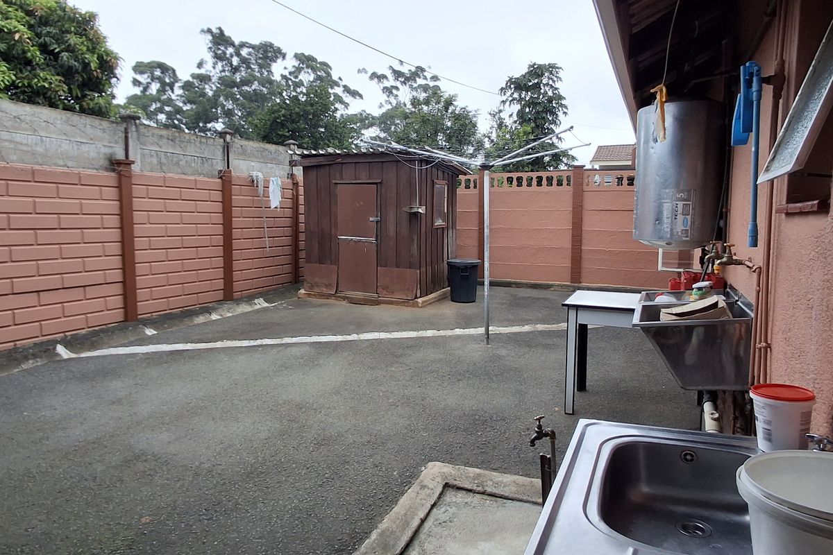 Rear yard area featuring a paved surface, precast boundary walls, a wooden storage shed, and an external utility sink with an electric water heater.