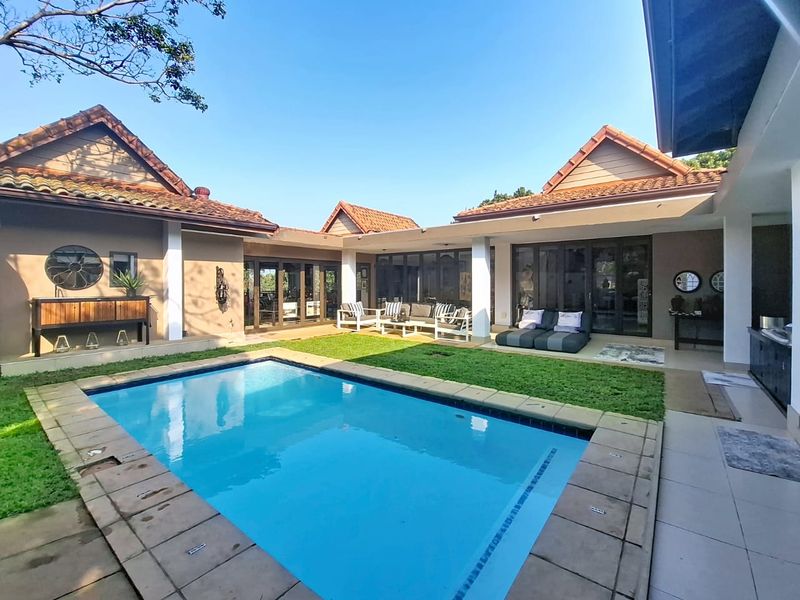 A spacious outdoor entertainment area featuring a swimming pool, a covered patio, and well-maintained garden space, perfect for relaxation and outdoor living.