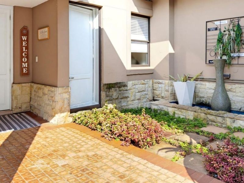 A welcoming front entrance area featuring stone cladding, a paved courtyard, and a raised garden bed.