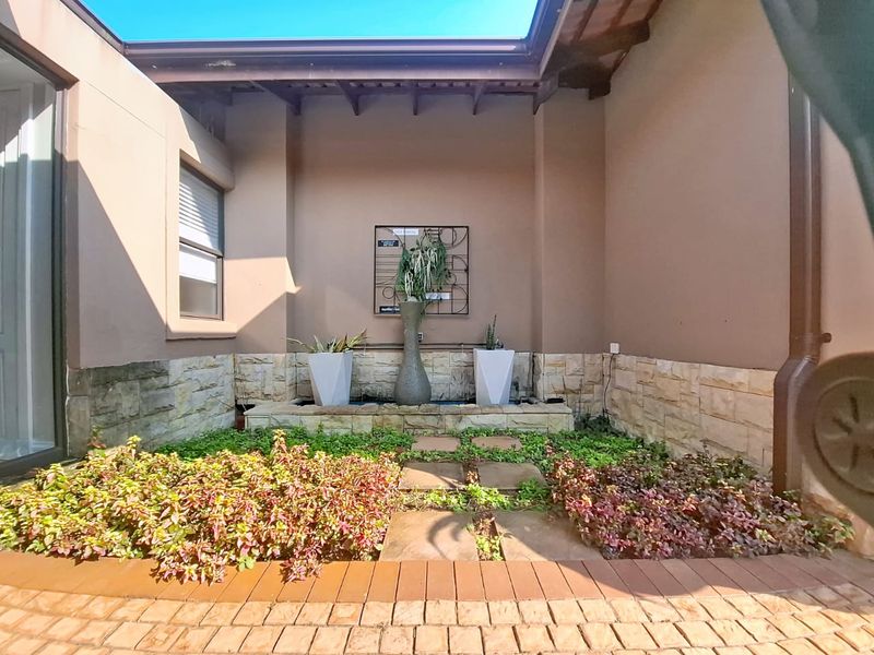 A private rear courtyard featuring a stone-clad water feature, paved walkway, and established garden beds under a timber pergola.