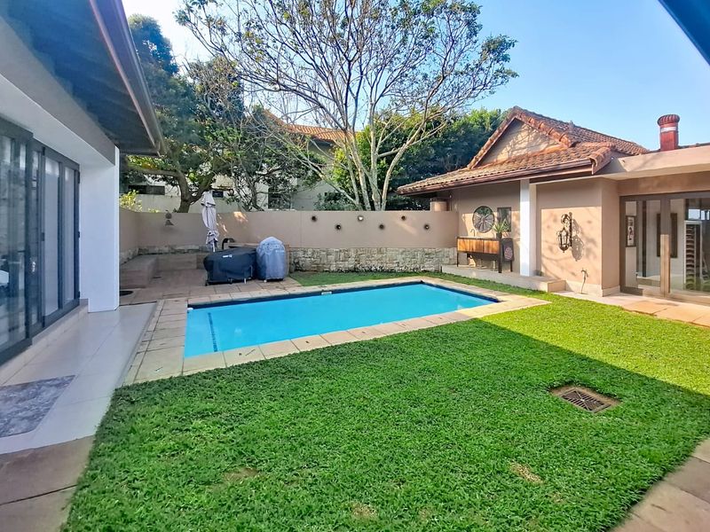 A well-maintained backyard featuring a swimming pool, manicured lawn, tiled patio area, and direct access to the home through large sliding glass doors.