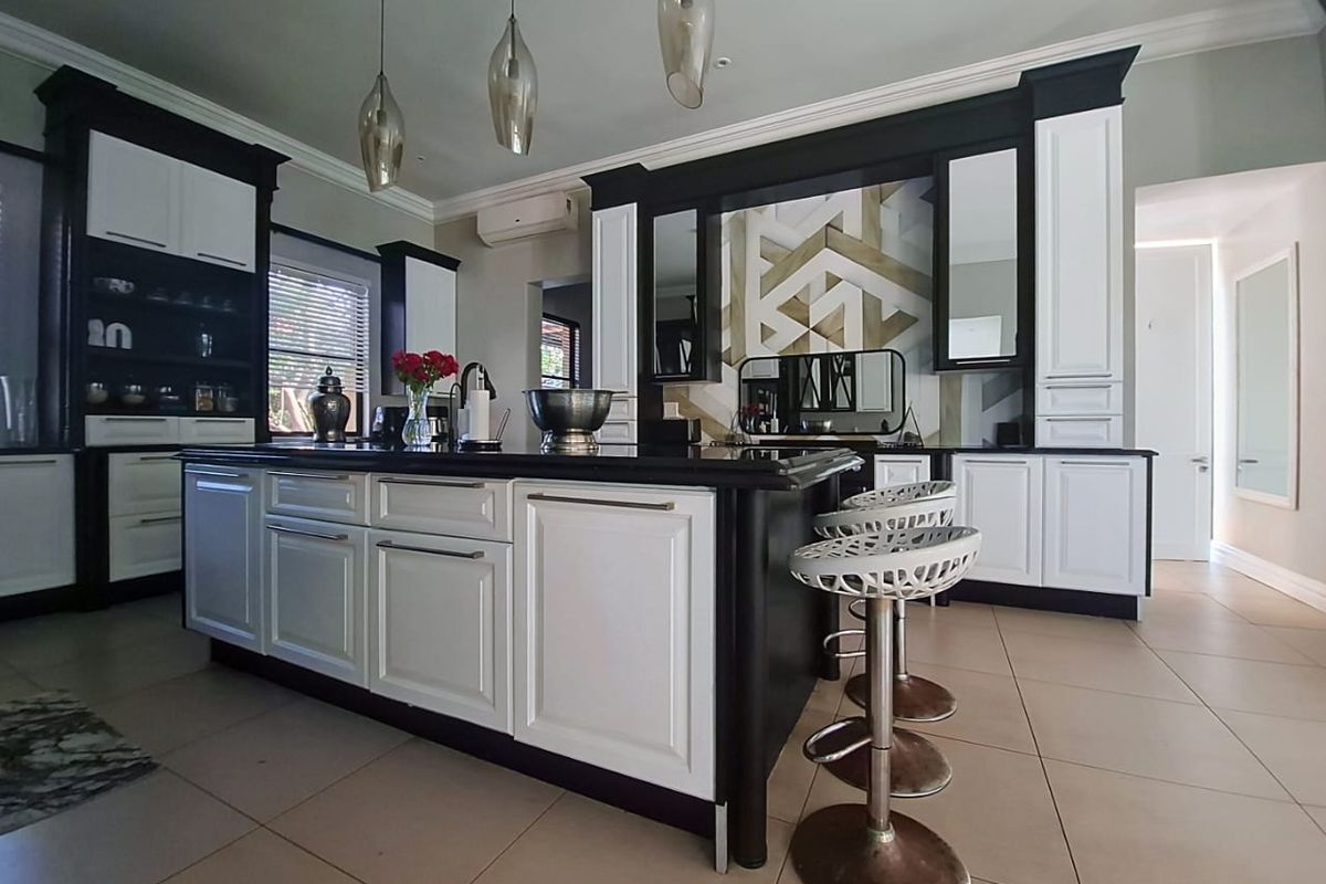 Modern kitchen featuring a large central island, high-contrast black and white cabinetry, decorative backsplash, and tiled flooring.